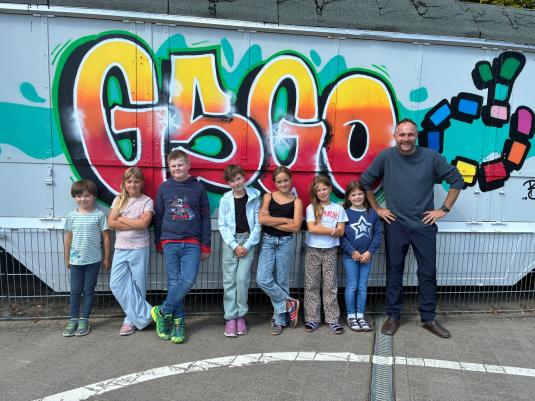 Die Schüler, welche sich um die Homepage kümmern, stehen zusammen mit Herr Rothenmeier vor einem Grafiti "GSGO"